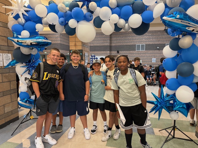 Six male students stand under Flyer balloon arch on the first day of school.