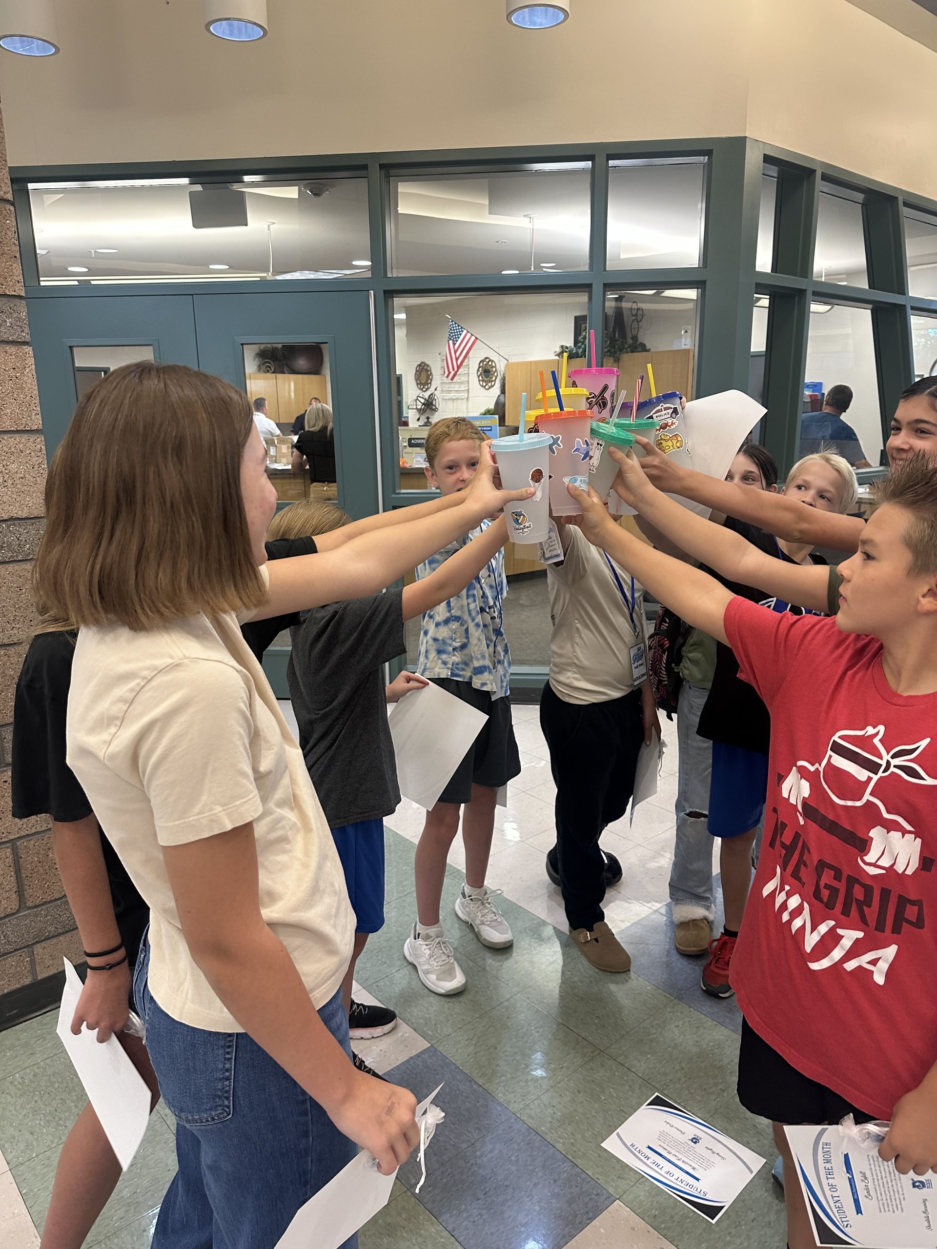 Eleven 6th and 7th graders show off their decorated drink tumblers outside the office.