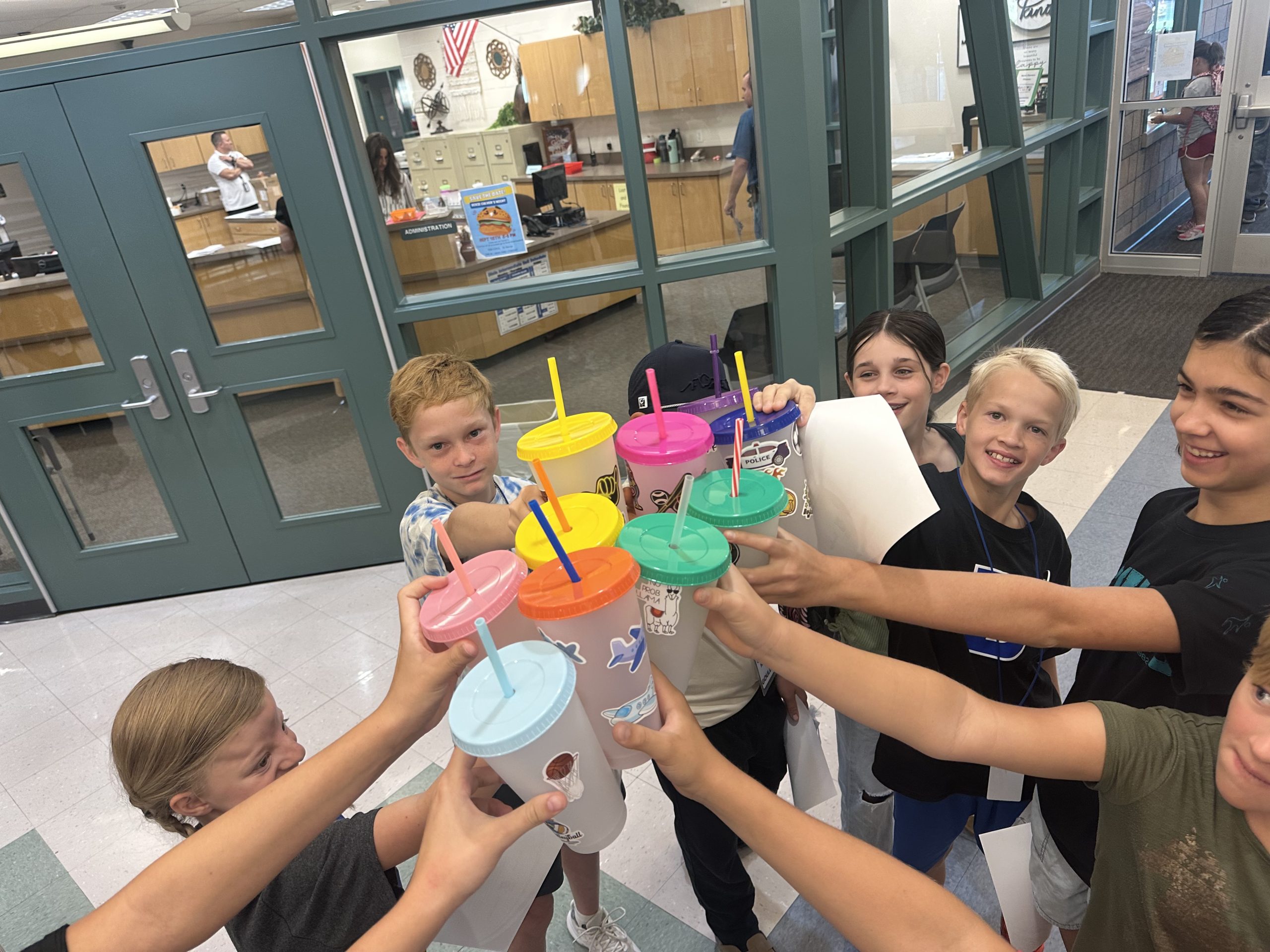 Eleven 6th and 7th graders show off their decorated drink tumblers outside the office.