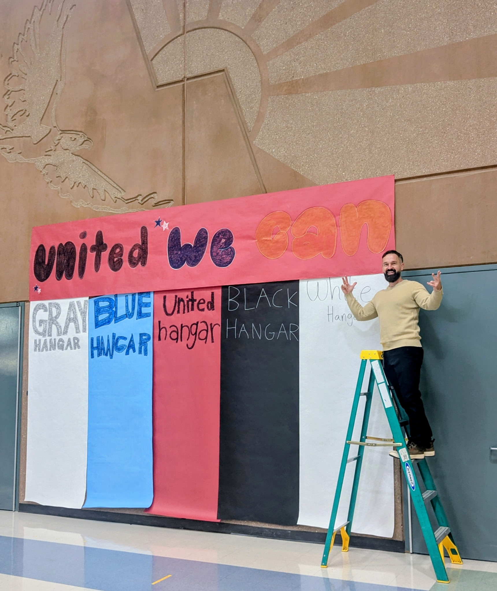 Mr. Tuttle on a ladder next to the 'United We Can' banner and bar graph for each hangar.